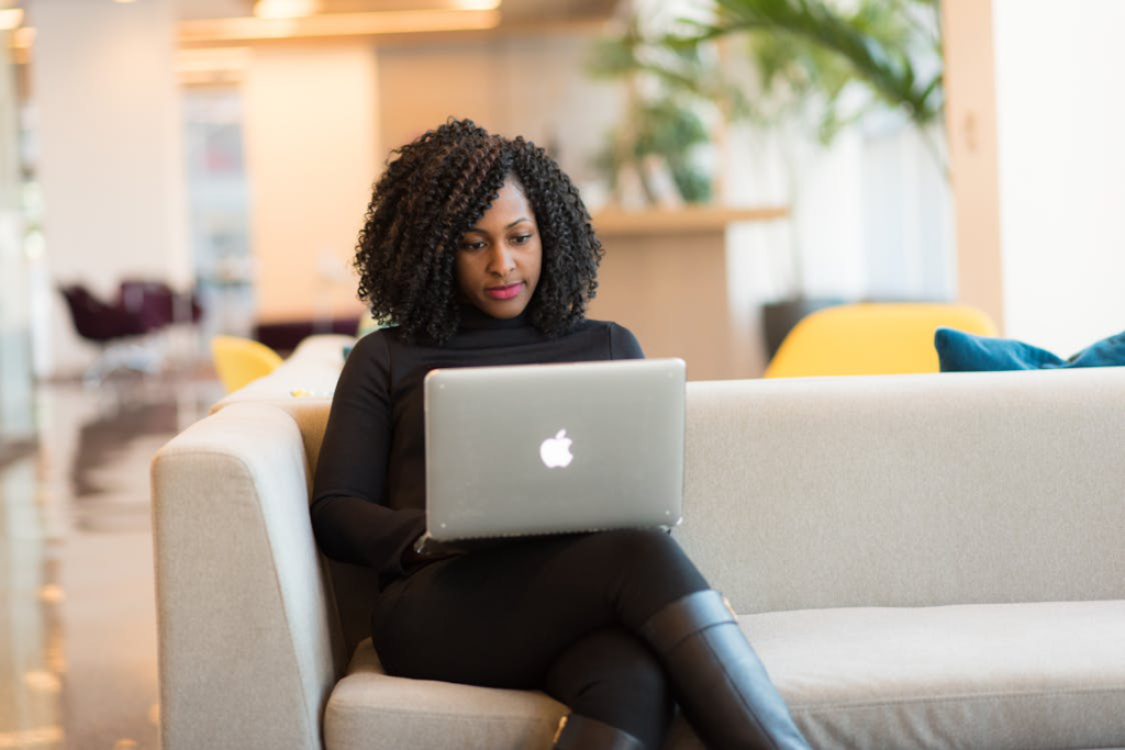 A woman is using a Macbook sitting on a white couch