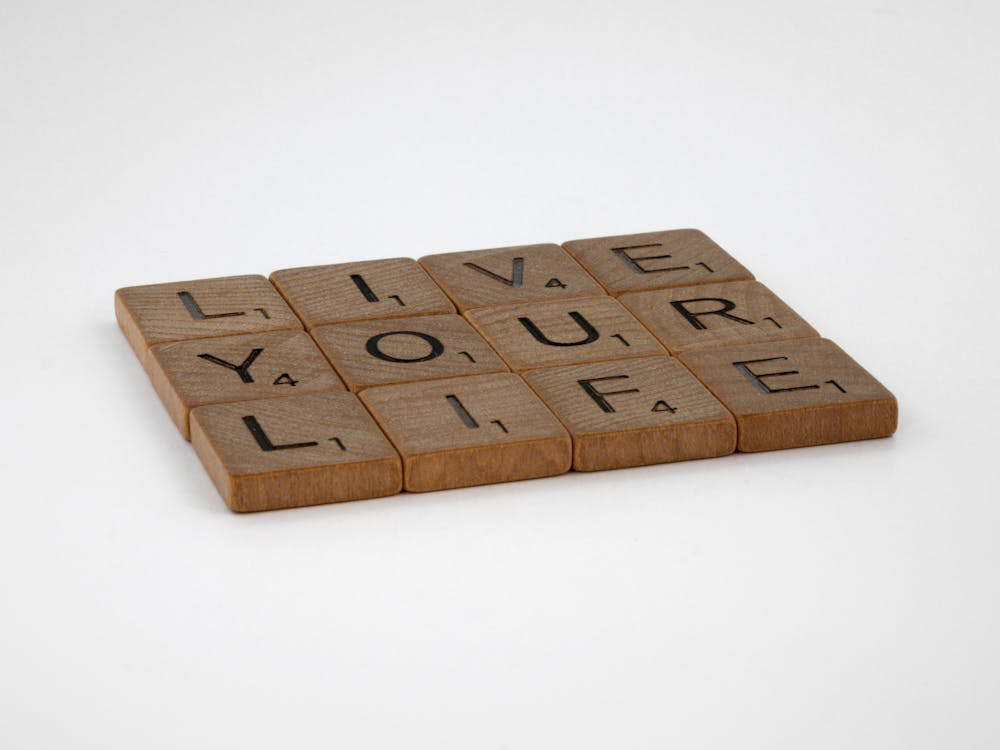 Scrabble tiles arranged on a white surface spell out the empowering message Live Your Life.