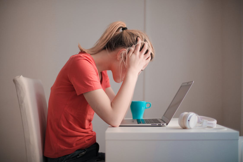 A woman in a red t-shirt looking at her laptop, feeling stressed