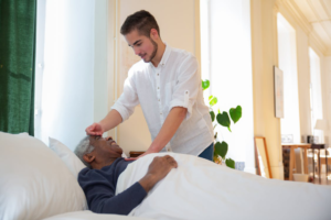 A man in a white shirt standing beside an elderly person lying on a hospital bed